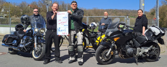 "Segel neu setzen!" steht auf einem Schild, das gehalten wird. Im Hintergrund stehen Motorräder.